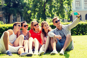 Image showing smiling friends with smartphone sitting on grass