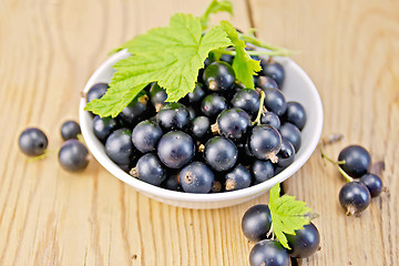 Image showing Black currants in bowl with leaf on board