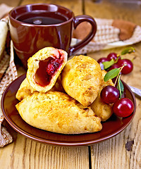 Image showing Pies with cherry and mug on board