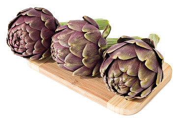 Image showing Three artichokes on a wooden plate