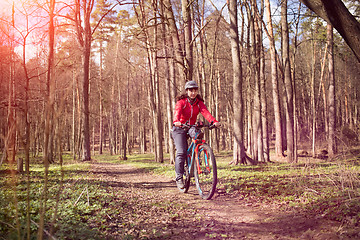 Image showing Young woman riding a bicycle through forest