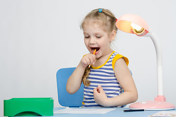 Image showing Happy little girl drawing a pencil stuck in her mouth