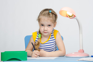 Image showing Girl sits at the table and draws a blue pencil