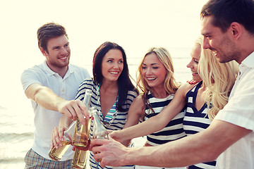 Image showing smiling friends clinking bottles on beach