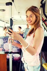 Image showing smiling teenage girl with smartphone going by bus