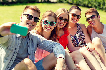 Image showing smiling friends with smartphone sitting on grass