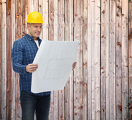 Image showing smiling male builder in helmet reading blueprint