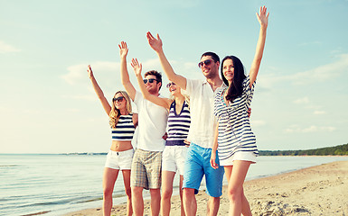 Image showing smiling friends walking on beach and waving hands