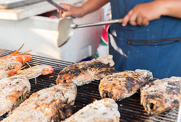 Image showing close up of cook hands grilling fish on street