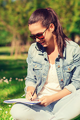 Image showing smiling young girl with notebook writing in park