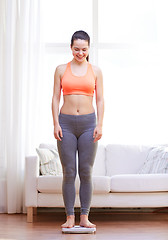 Image showing happy young woman weighing on scales at home