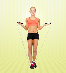 Image showing smiling sporty woman jumping with skipping rope