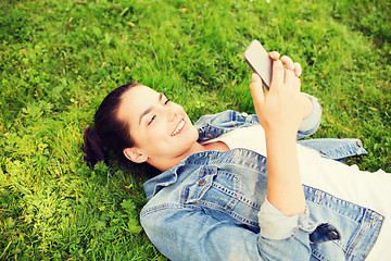 Image showing smiling young girl with smartphone lying on grass