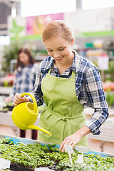 Image showing happy woman with watering can in greenhouse