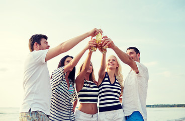 Image showing smiling friends clinking bottles on beach