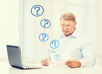 Image showing old man in eyeglasses filling a form at home