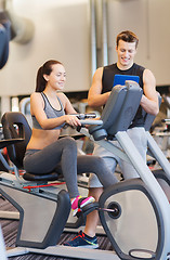 Image showing happy woman with trainer on exercise bike in gym