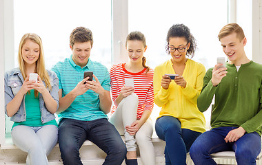 Image showing smiling students with smartphone texting at school