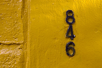 Image showing  old black numbers  in a yellow wall 