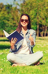Image showing smiling young girl with book sitting on grass