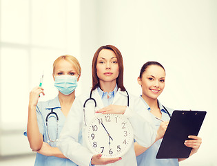 Image showing calm female doctor and nurses with wall clock