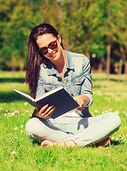 Image showing smiling young girl with book sitting in park