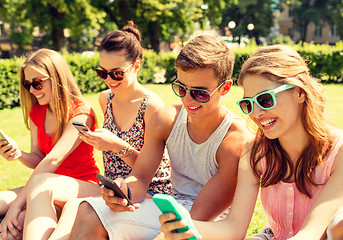 Image showing smiling friends with smartphones sitting on grass