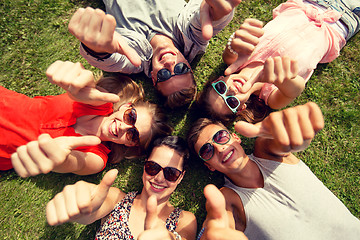 Image showing smiling friends showing thumbs up lying on grass