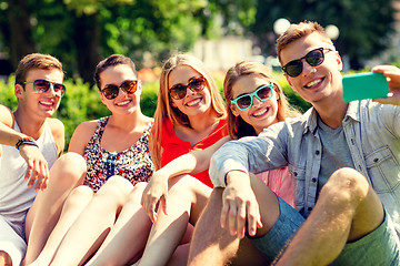 Image showing smiling friends with smartphone sitting on grass