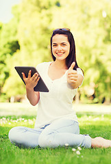 Image showing smiling young girl with tablet pc sitting on grass