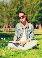 Image showing smiling young girl with notebook writing in park