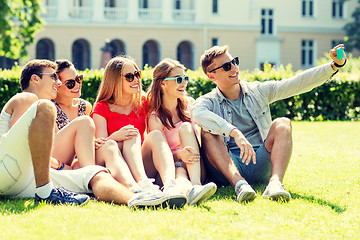 Image showing smiling friends with smartphone sitting on grass