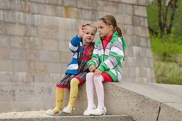 Image showing Girl shows something other girl, sitting on a granite ramp