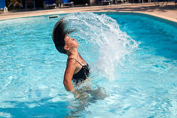 Image showing Pretty teen girl whipping her hair back in the pool and spraying water everywhere