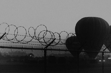 Image showing grainy dramatic image of hot air balloons behind barbed wire fence