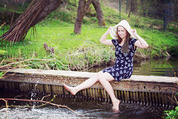 Image showing Cheerful fashionable woman sits on small bridge and splashing wa