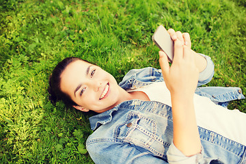 Image showing smiling young girl with smartphone lying on grass