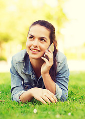 Image showing smiling young girl with smartphone lying on grass