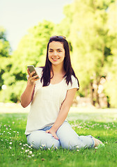 Image showing smiling young girl with smartphone sitting in park