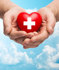 Image showing male hands holding red heart with white cross