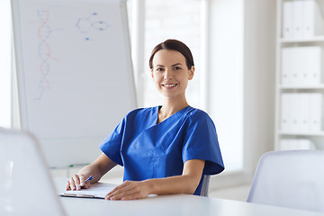 Image showing happy female doctor or nurse writing to clipboard