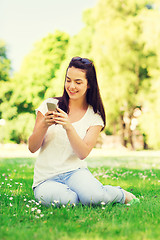 Image showing smiling young girl with smartphone sitting in park
