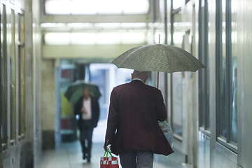 Image showing Senior adults with umbrellas in passage