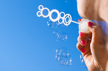 Image showing Female person blowing soap bubbles into blue sky