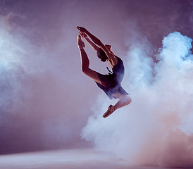 Image showing Beautiful young ballet dancer jumping on a lilac background. 