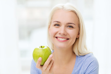 Image showing happy woman eating green apple at home