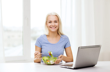 Image showing smiling woman eating salad with laptop at home