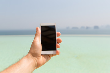 Image showing close up of male hand holding smartphone on beach