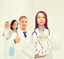 Image showing calm female doctor with wall clock