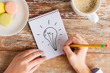 Image showing close up of hands drawing bulb to notebook